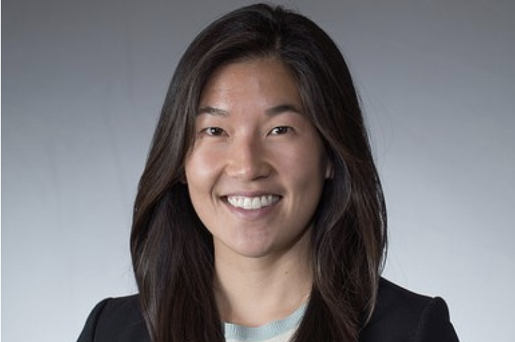 Headshot of a woman smiling, wearing a blazer against a gray background
